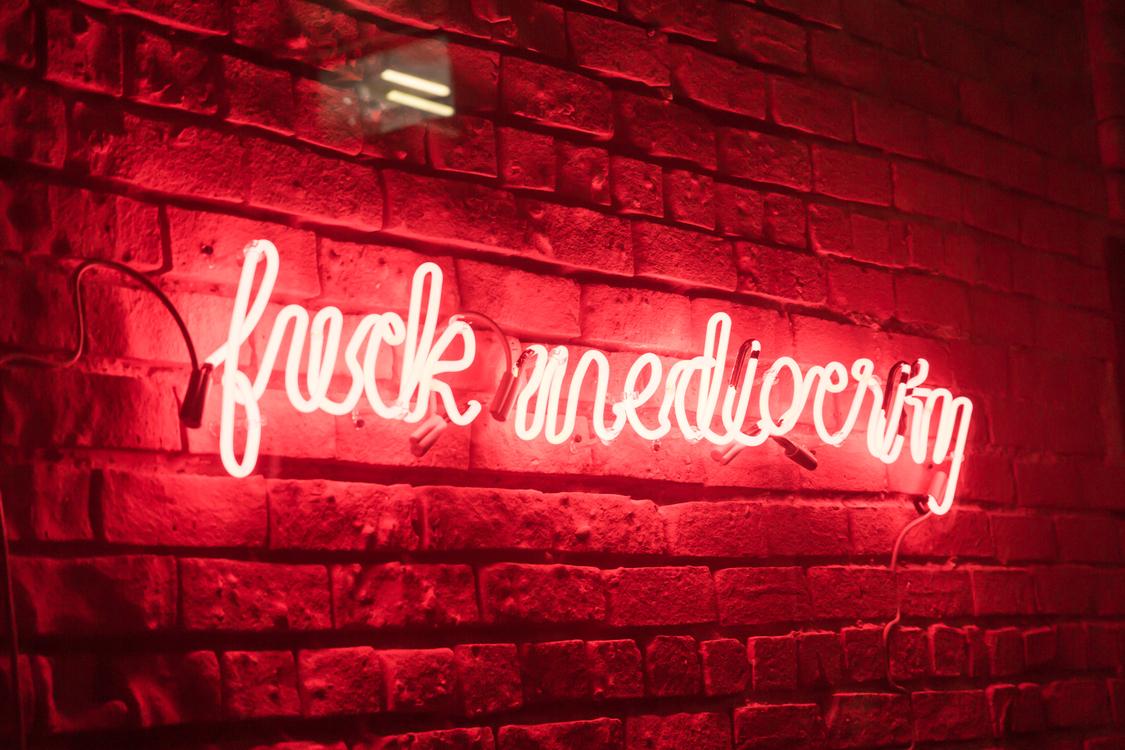 Fuck Mediocrity, Neonschrift, Backsteinwand, Rot, Hintergrund