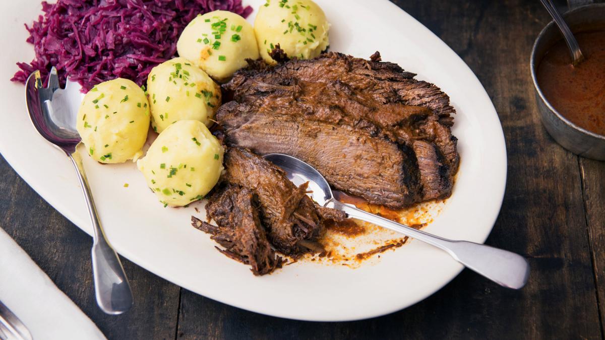 Sauerbraten, Salzkartoffeln, Rotkohl, Soßenkännchen, Holztisch, Hintergrundbild